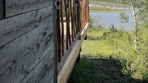 A wooden cabin with a balcony overlooking a lake and forested hills.