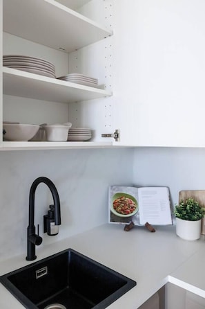 A kitchen with white shelves, a black sink, and a cookbook. - Skyline Suite · Danube View Balcony · Pool · Metro (Wien)