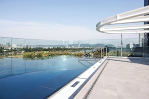 Piscina no terraço com vista para a cidade, guarda-corpo de vidro e design arquitetônico moderno.