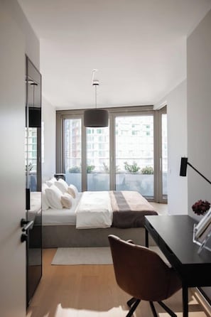 Um quarto moderno com cama, escrivaninha, cadeira e janelas amplas.