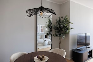 A modern living room with a round dining table, a sofa, a TV stand, and a large mirror. - Skyline Suite · Danube View Balcony · Pool · Metro (Wien)