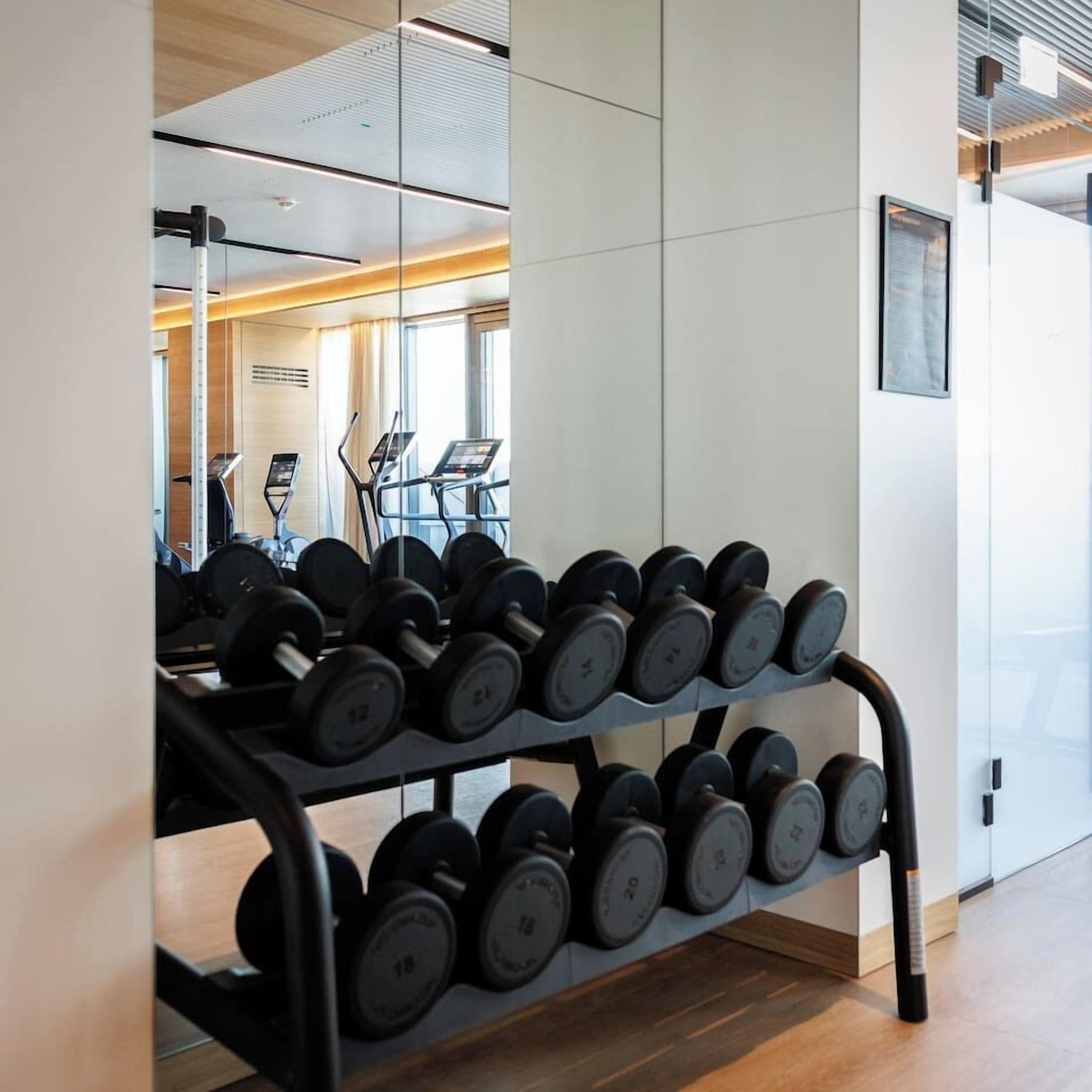 Ein Fitnessstudio mit Hantelbank, Laufband und Spiegelwand.