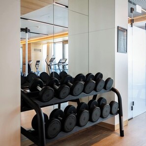 A gym with a rack of dumbbells, a treadmill, and a mirrored wall.
