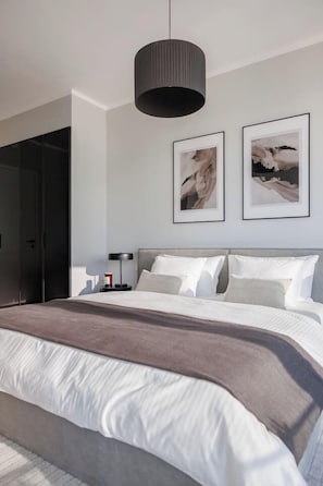 A modern bedroom with a large bed, a bedside table with a lamp, and two framed artworks on the wall. - Skyline Suite · Danube View Balcony · Pool · Metro (Wien)