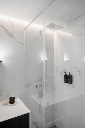 Um banheiro moderno com chuveiro em box de vidro, paredes de mármore e toucador branco.