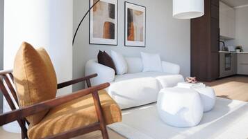 Ein modernes Wohnzimmer mit Sofa, Hocker und Sessel, im Hintergrund eine Küche und zwei abstrakte Gemälde an der Wand.
