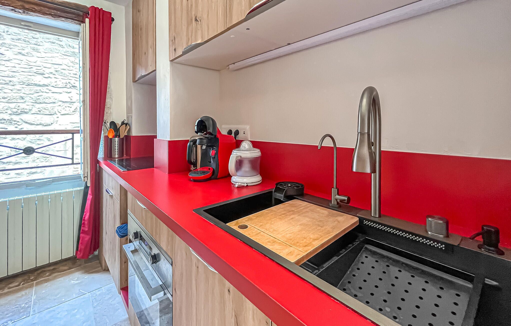 Une cuisine moderne avec un plan de travail rouge, une machine à café, une bouilloire et un évier.