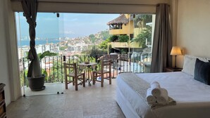 A hotel room with a balcony, a bed, a table with chairs, and a view of the cityscape.