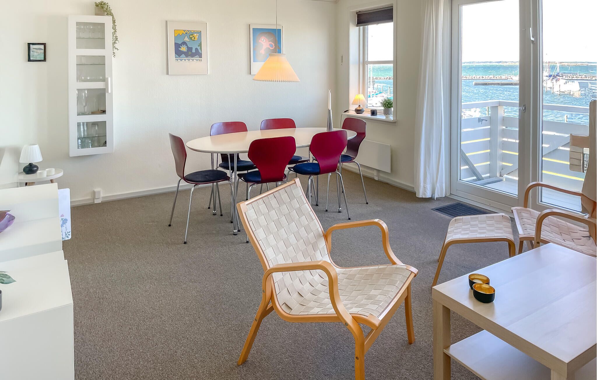 A modern hotel room with a dining area, a large window with a view of the sea, and a balcony.