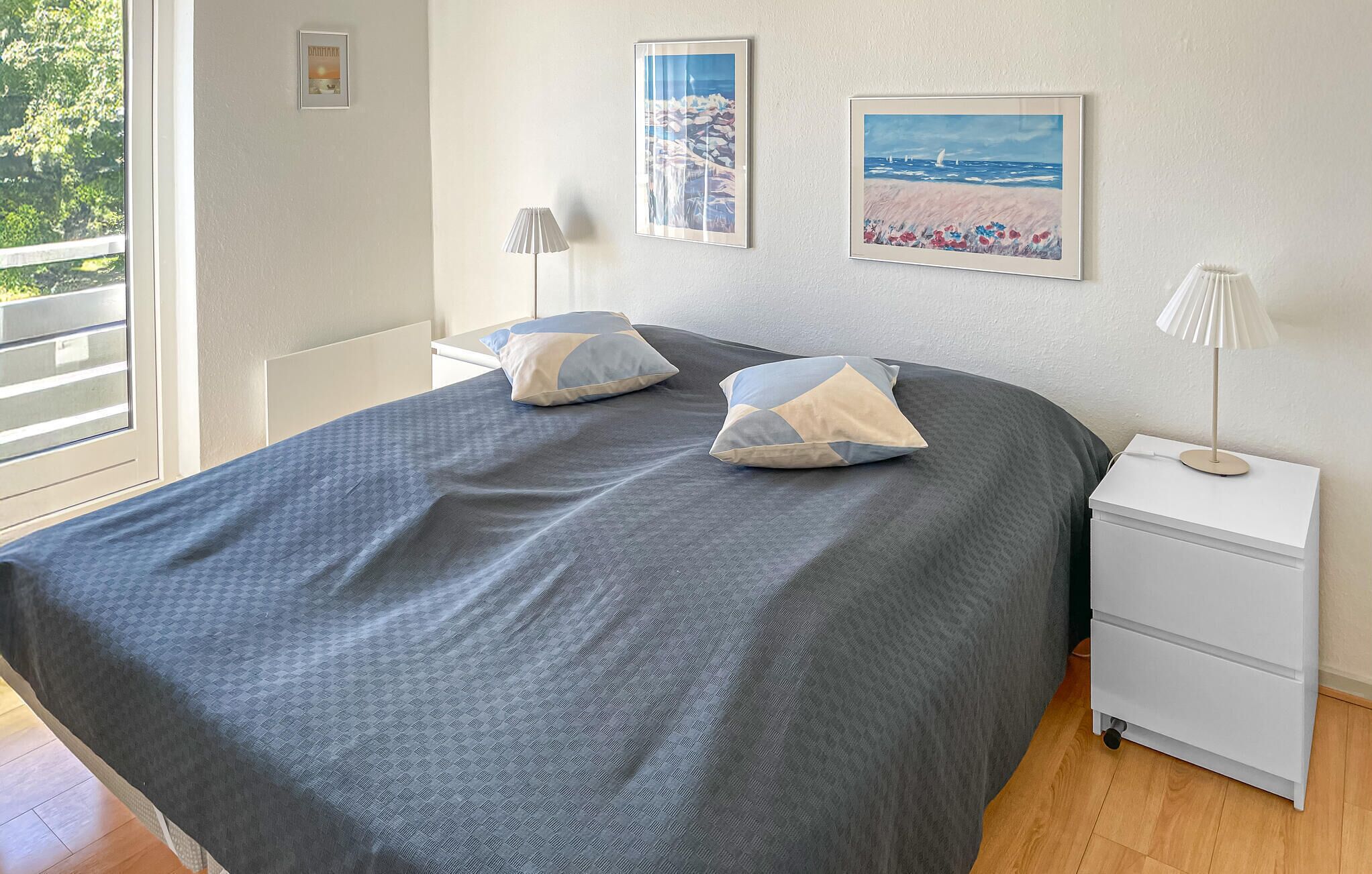 A bedroom with a large bed, two bedside lamps, a nightstand, and two framed pictures on the wall.