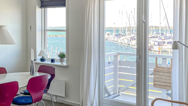 A room with a dining table, chairs, a window with a view of the marina, and a door leading to a balcony. - Lovely apartment in Rudkøbing with house sea view (Rudkøbing)