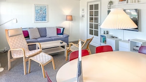 A modern living room with a sofa, chairs, a dining table, a lamp, and a TV.
