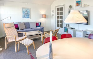 A modern living room with a sofa, chairs, a dining table, a lamp, and a TV.