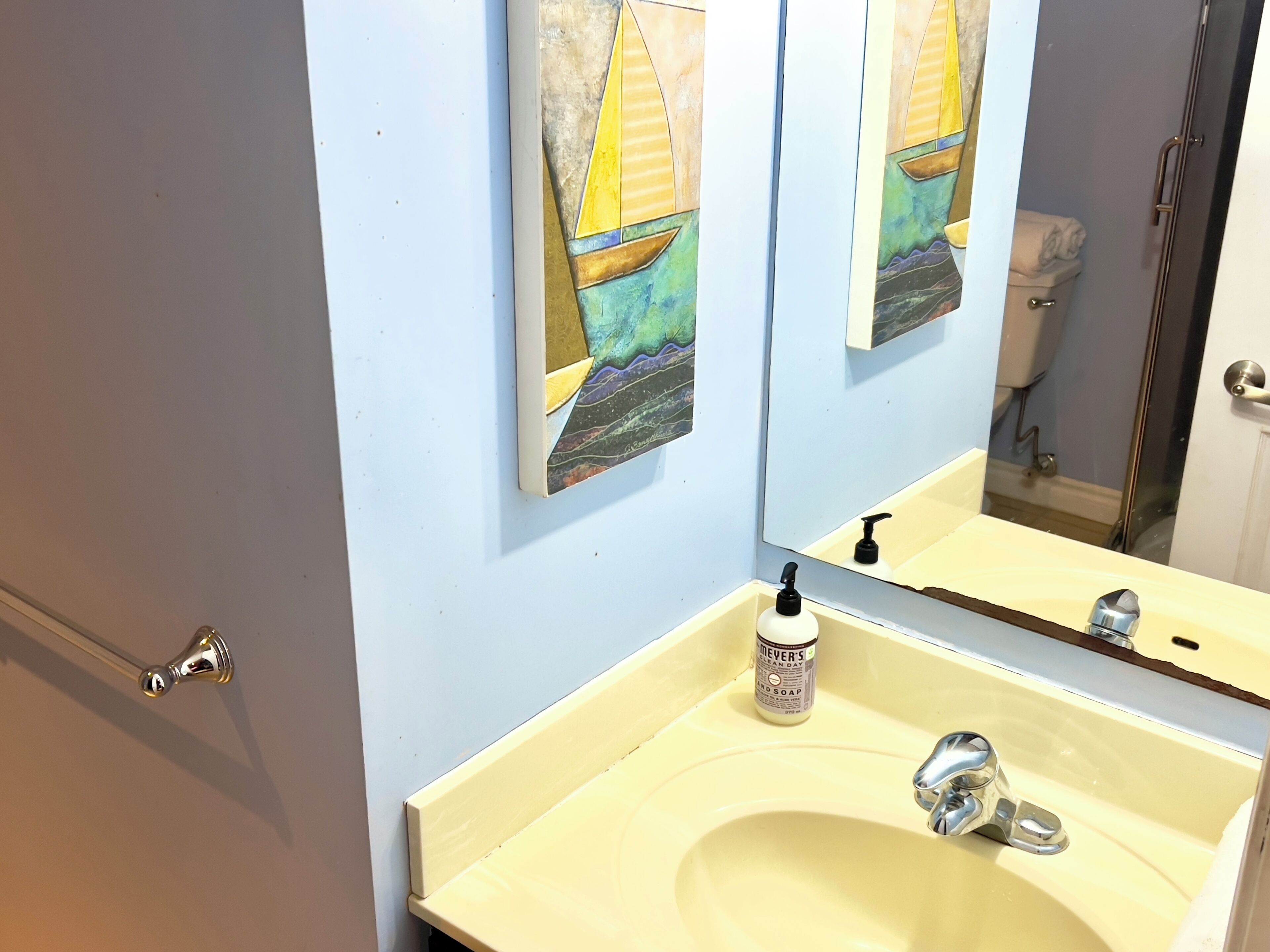 Un bagno con lavandino, specchio e un quadro raffigurante una barca a vela appeso al muro.