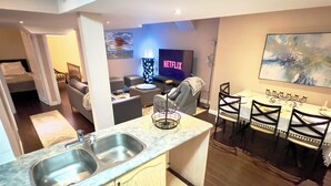 Une chambre d’hôtel moderne dotée d’une kitchenette, d’un coin repas avec une table et des chaises, d’un canapé, d’une télévision et d’un tableau au mur.