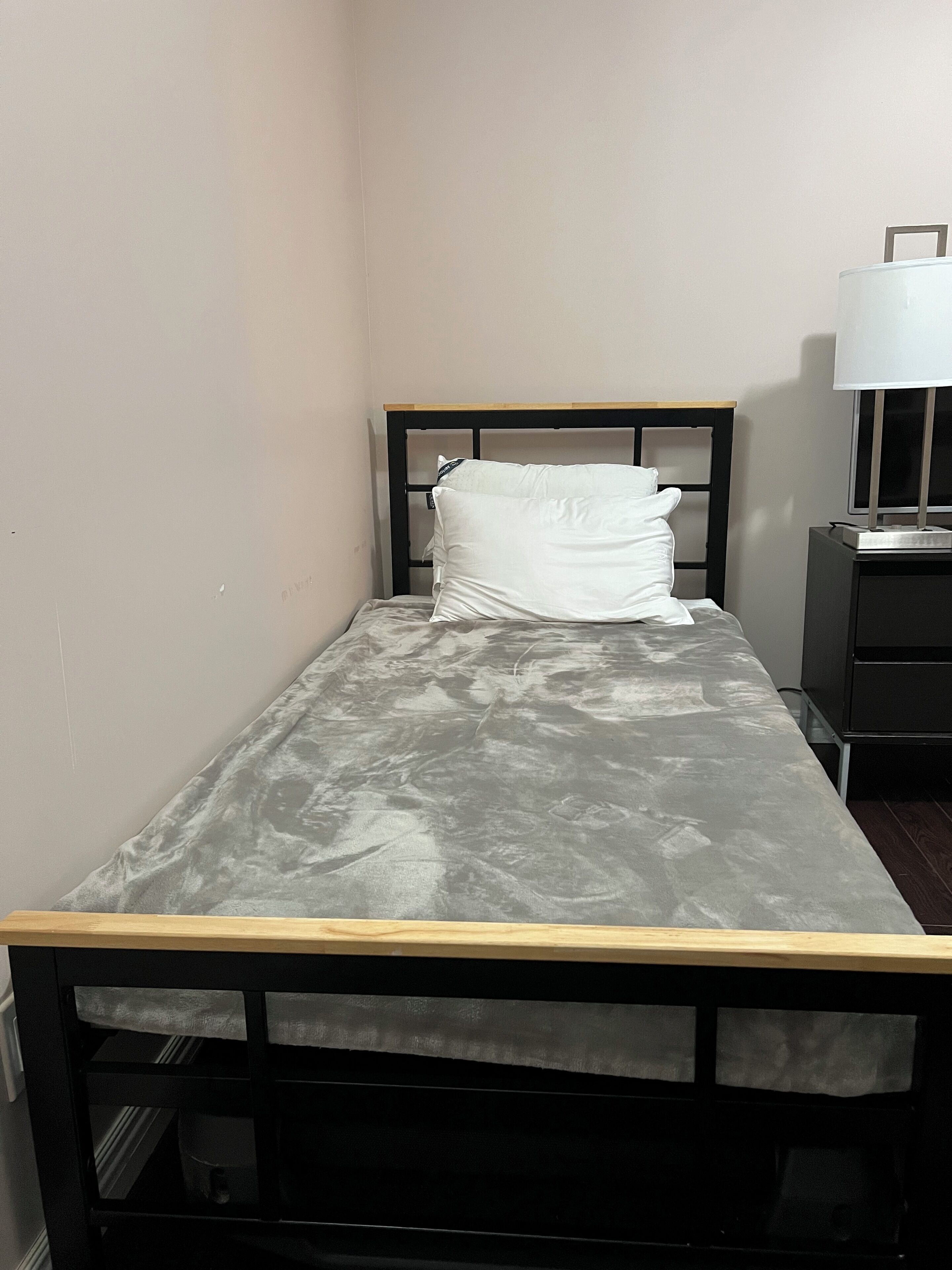 A small, single-bed room with a wooden headboard, a white pillow, and a bedside table with a lamp.