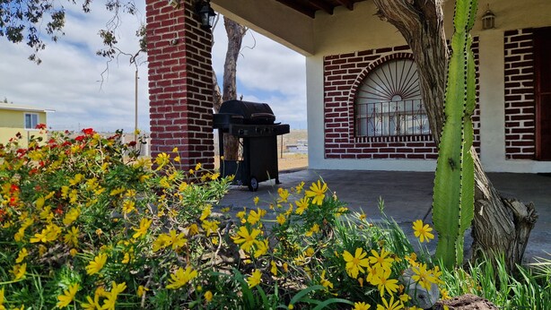 A covered patio with a brick chimney, a grill, and a window with decorative bars. - Excellent 2-bedroom house near Rosarito Beach (Rosarito)