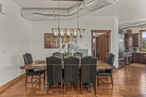 Un vaste espace dédié à la salle à manger, avec une table et des chaises en bois, un lustre et une vue sur la cuisine.