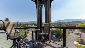 Un balcon avec deux chaises et une table, donnant sur un parking et sur des montagnes lointaines.