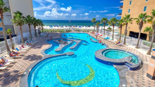 A pool area with multiple swimming pools, palm trees, and a beach view.
