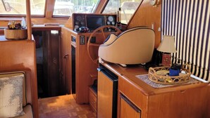 A boat's interior with a wooden dashboard, steering wheel, and a small table with a lamp and a basket. - 2 Cabin Classic Yacht in Petoskey's Bay Harbor (Petoskey)