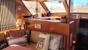A cozy cabin with a wooden interior, a cushioned seating area, a small table with a lamp, and a window offering a view of the outside. - 2 Cabin Classic Yacht in Petoskey's Bay Harbor (Petoskey)