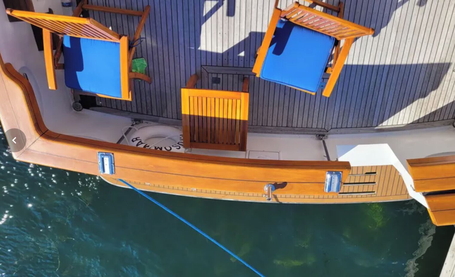 A boat with a wooden deck, two blue cushioned seating areas, and a small table.