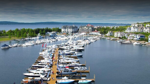 A marina with numerous boats docked along a wooden pier, surrounded by residential buildings and a backdrop of hills and a body of water. - 2 Cabin Classic Yacht in Petoskey's Bay Harbor (Petoskey)