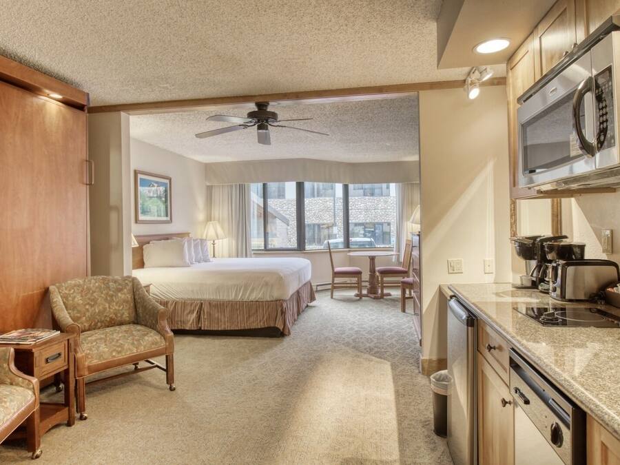 A hotel room with a bed, a chair, a desk, a microwave, and a coffee maker.