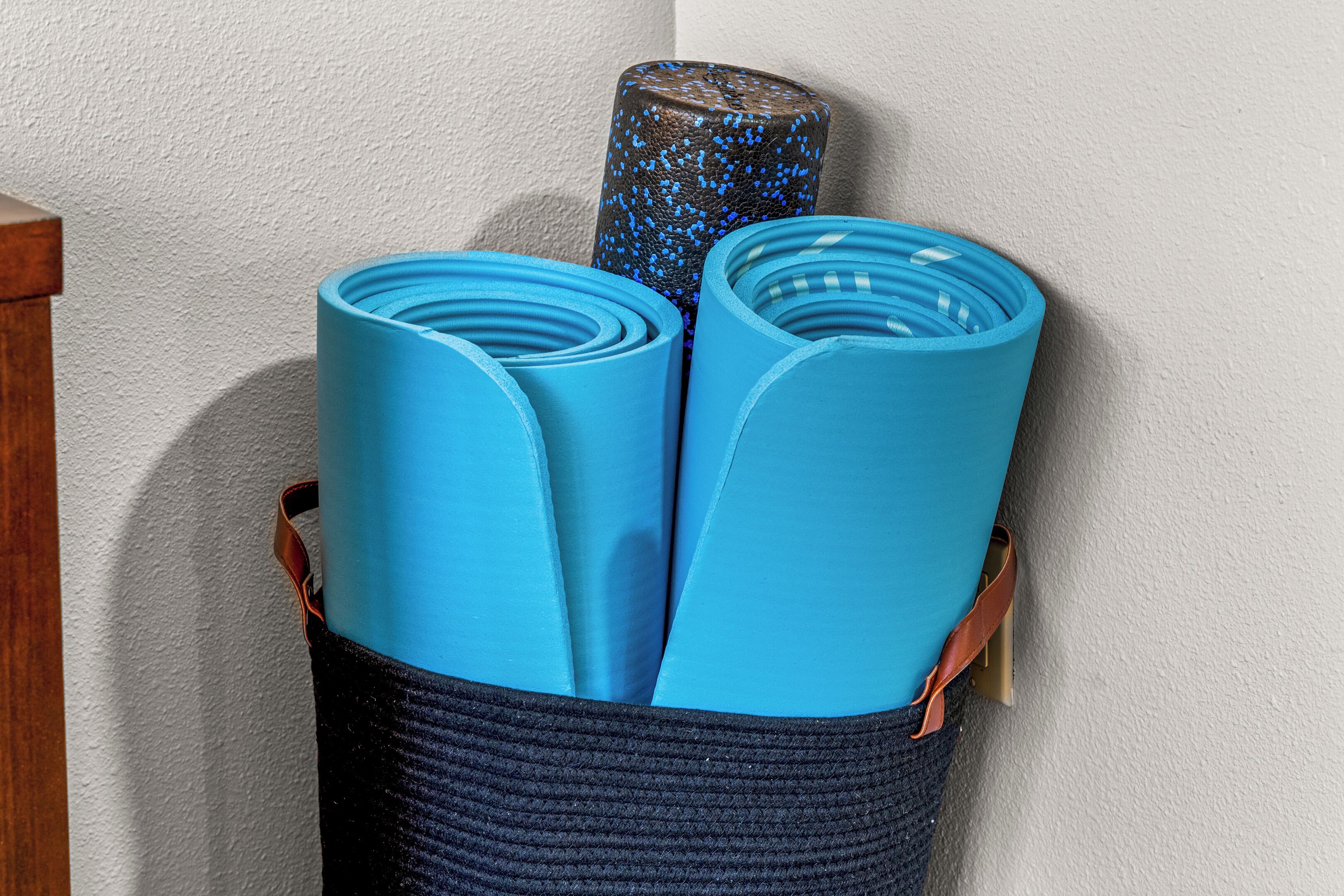 A basket containing several blue yoga mats and a textured cylindrical object.