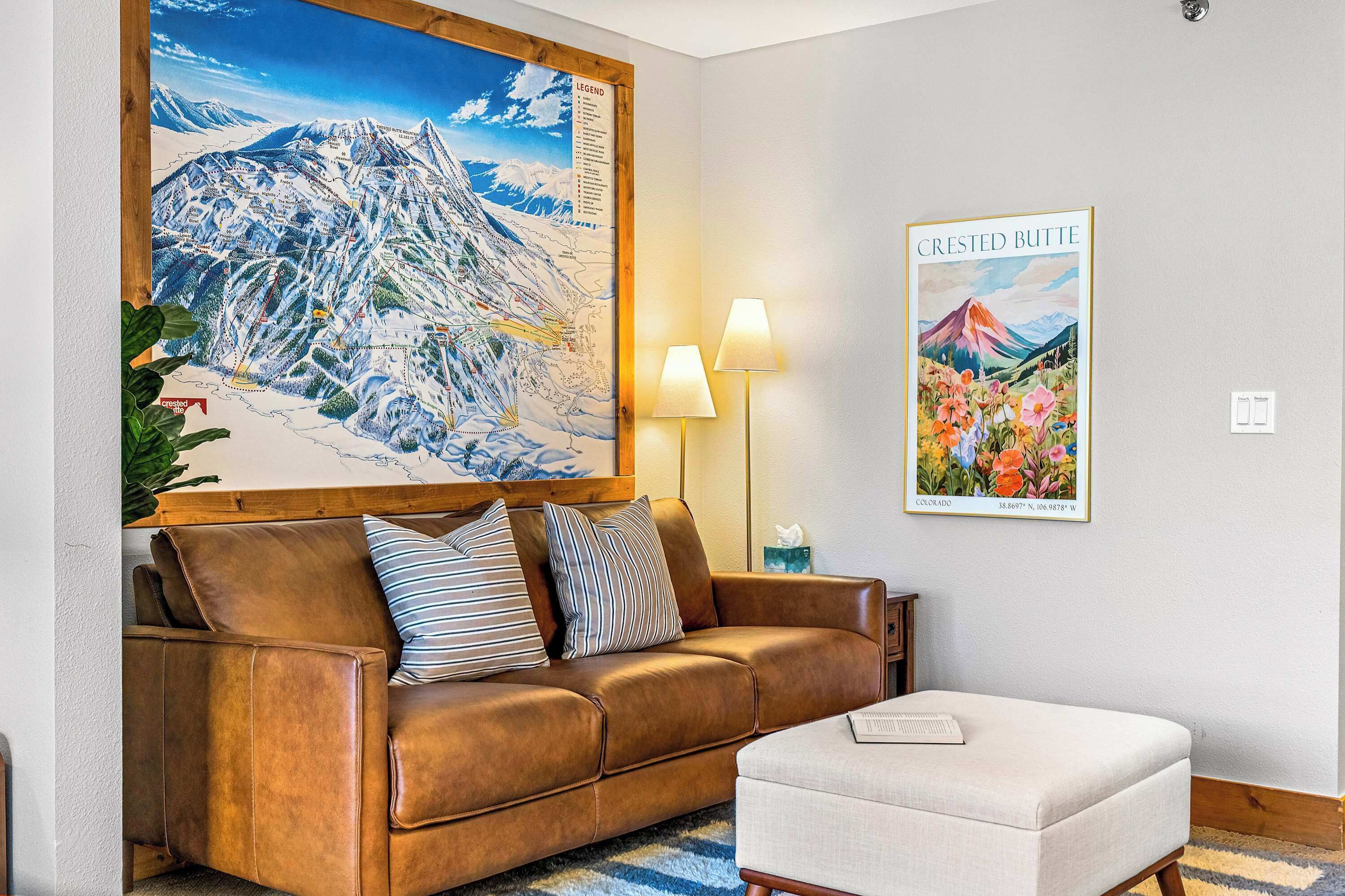 A cozy living room with a brown leather sofa, a white ottoman, and a large wall map.