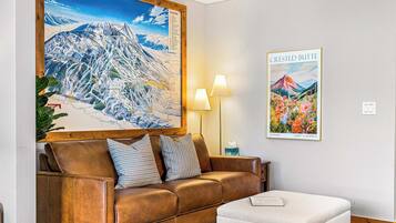 A cozy living room with a brown leather sofa, a white ottoman, and a large wall map.