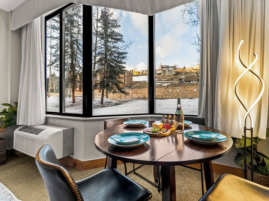 A dining area with a large window, a table set with plates and a fruit bowl, and a modern light fixture.