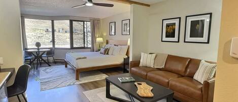 A modern living room with a bed, a leather sofa, a coffee table, and a dining area with a table and chairs.