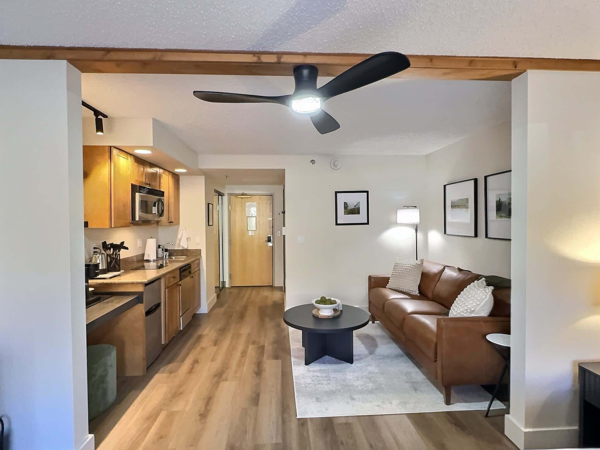 A modern living room with a brown leather sofa, a round coffee table, and a ceiling fan.