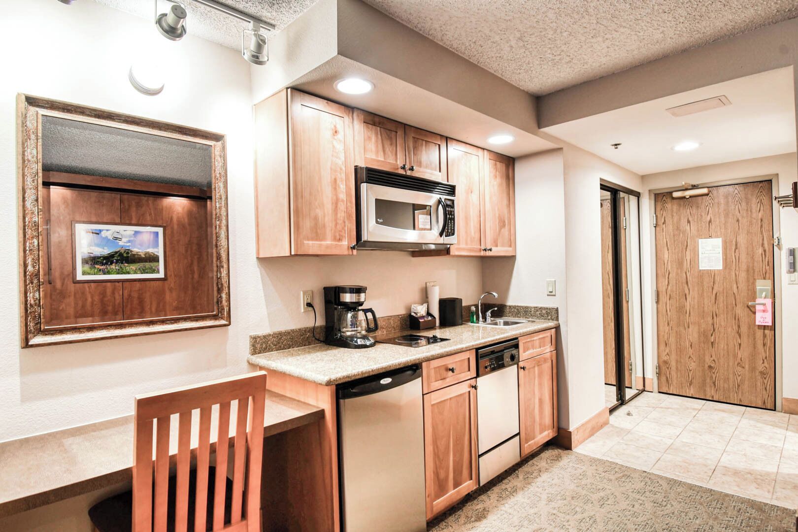 A compact kitchen with wooden cabinets, a built-in microwave, a coffee maker, and a dishwasher.