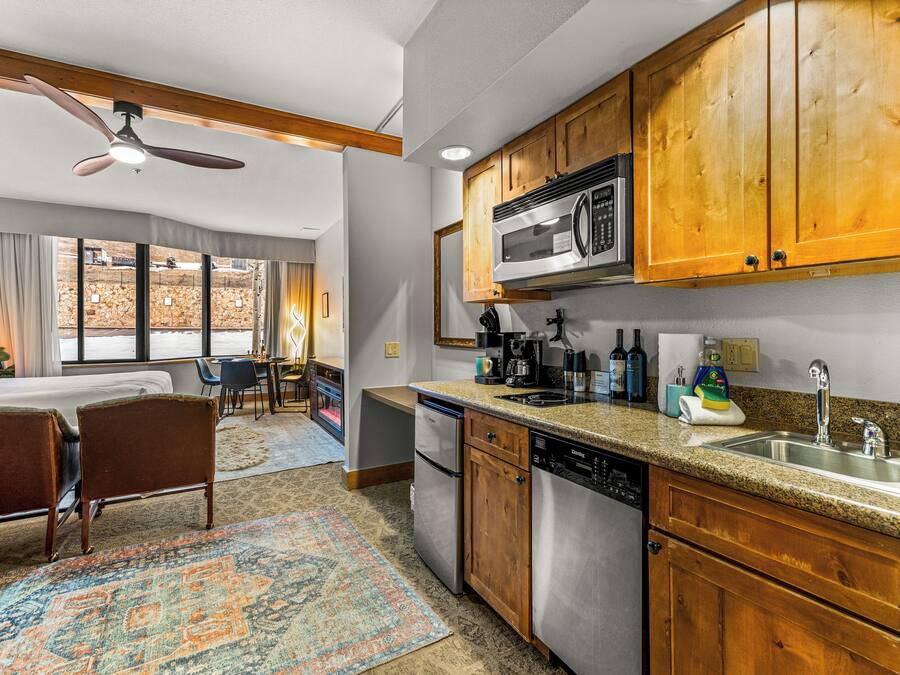 A kitchen with wooden cabinets, a microwave, a dishwasher, and a sink. There is a dining area with chairs and a rug.