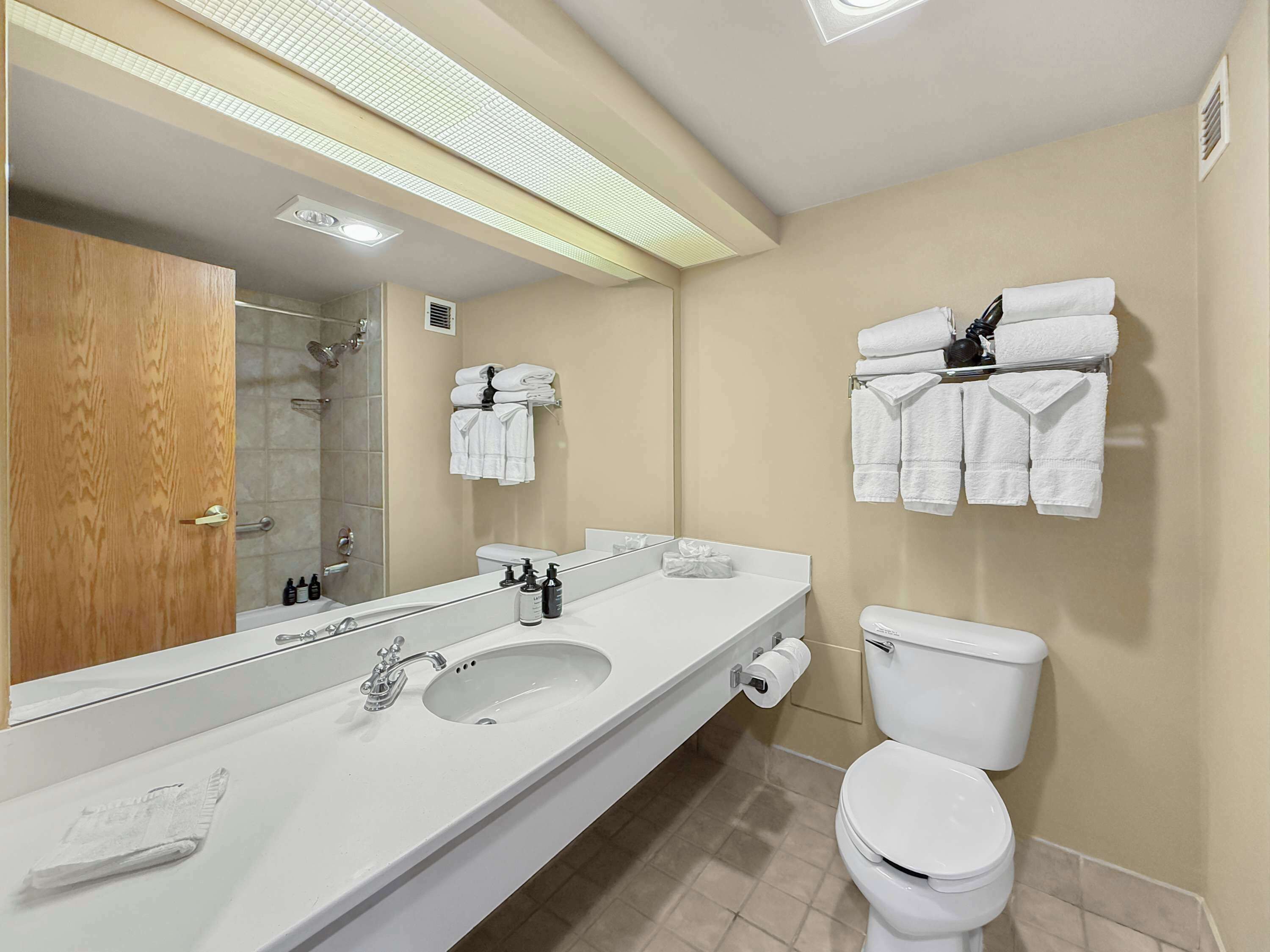 A modern bathroom with a large mirror, a sink, a toilet, and towel racks.