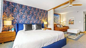 A bedroom with a large bed, a ceiling fan, a nightstand with a lamp, a wooden dresser, and a painting on the wall.