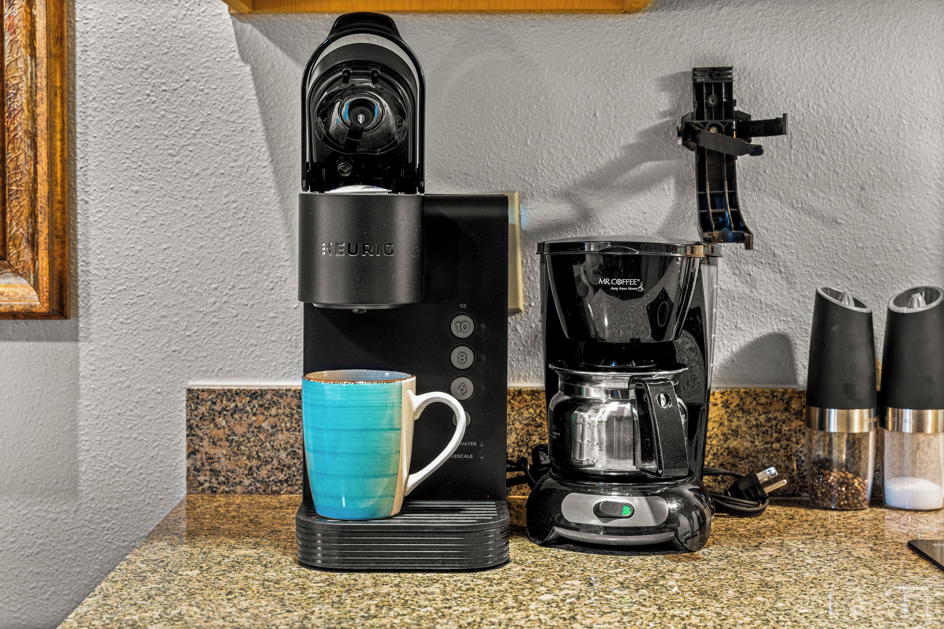A coffee maker with a blue mug on a granite countertop.