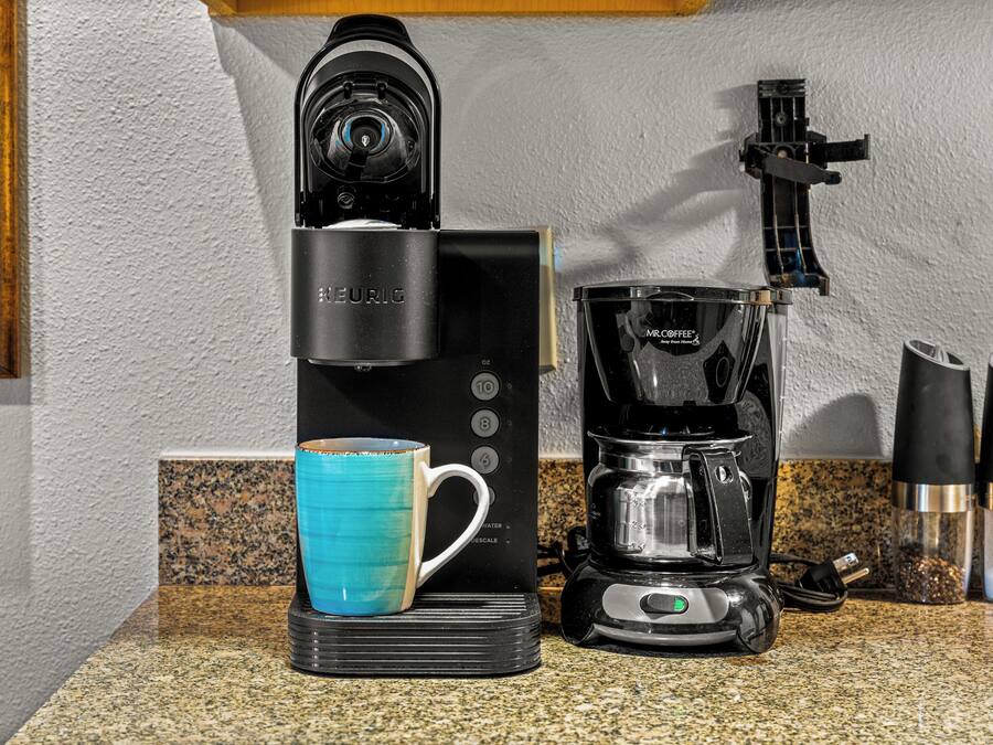 A coffee maker with a blue mug on a granite countertop.