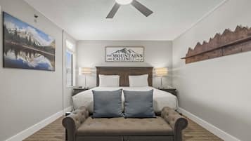 Ein Schlafzimmer mit einem Bett, zwei Nachttischlampen, einem Deckenventilator, einem Bergmotiv und einer Holzablage mit Haken.