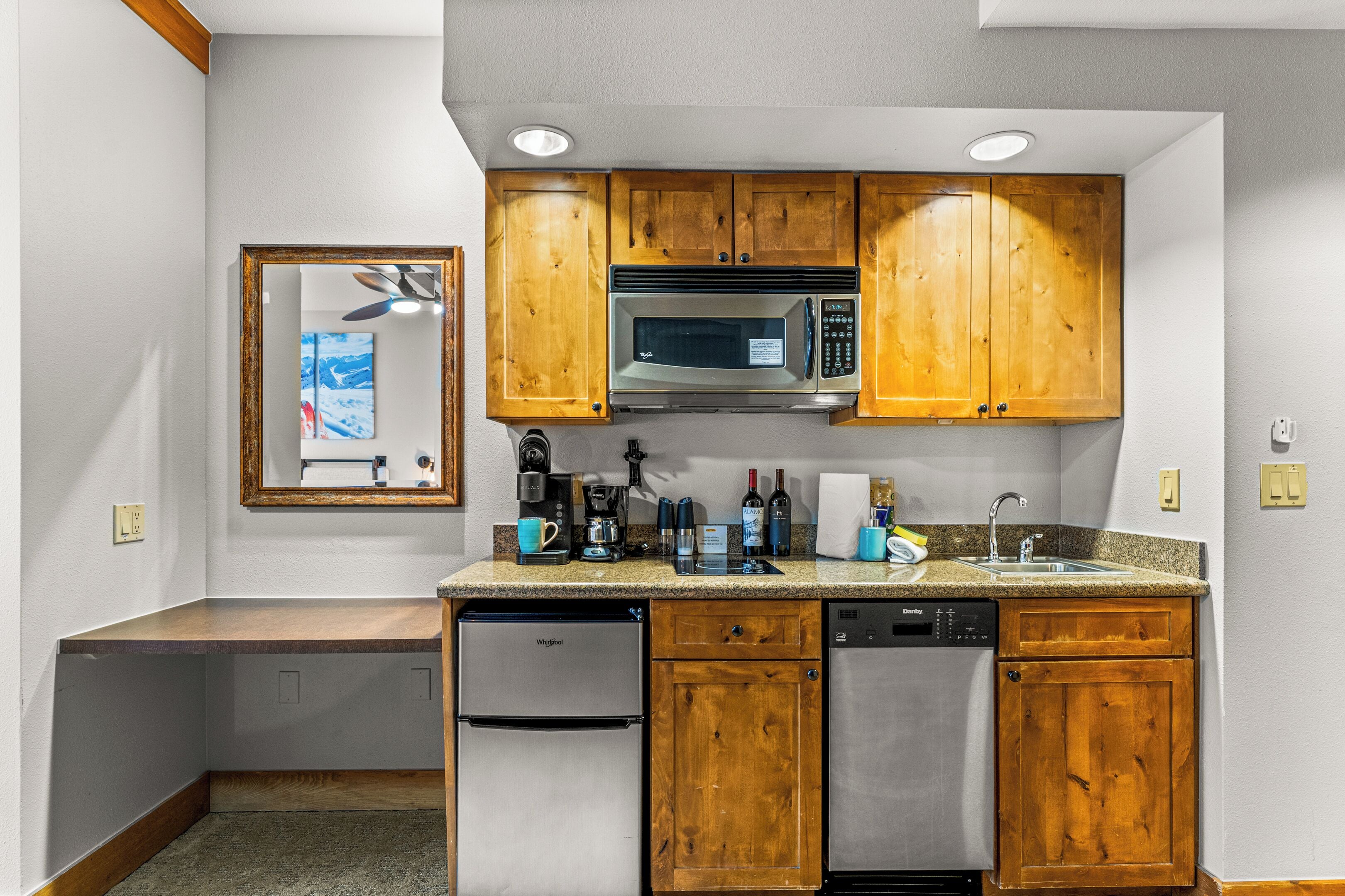 A compact kitchen with wooden cabinets, a microwave, a coffee maker, and a dishwasher.