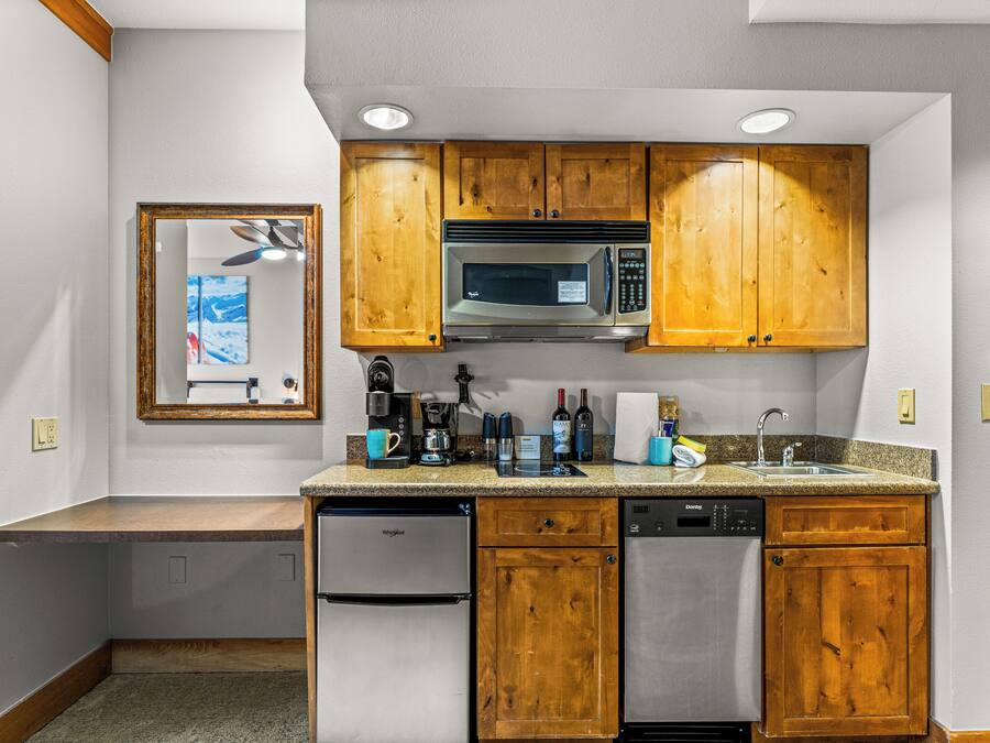A compact kitchen with wooden cabinets, a microwave, a coffee maker, and a dishwasher.