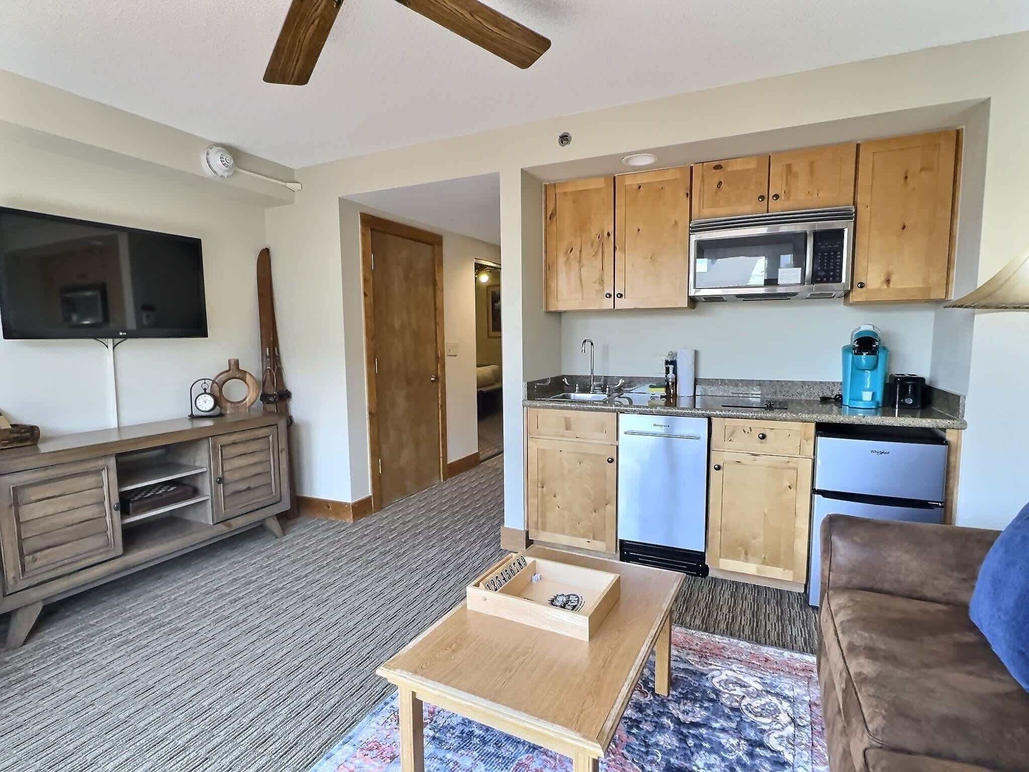 A compact living space with a kitchenette, a television, a wooden cabinet, and a small table.
