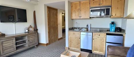 A compact living space with a kitchenette, a television, a wooden cabinet, and a small table.