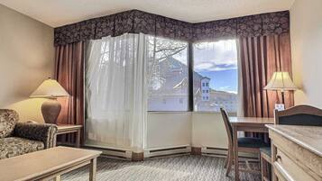 Habitación de hotel con un ventanal grande, un escritorio, una silla, un sofá y dos lámparas.