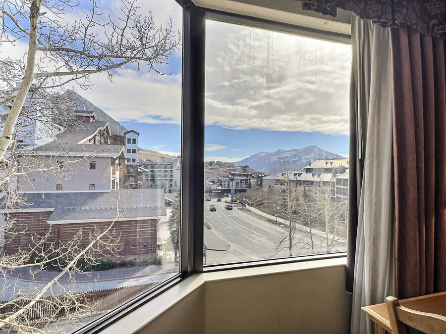 A room with a large window offering a view of a cityscape, including buildings and mountains.