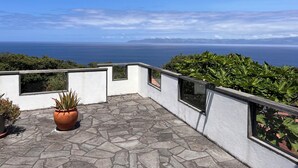 A terrace with a stone floor, potted plants, and a view of the sea and distant mountains.