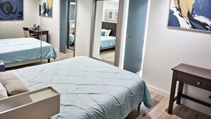 A modern bedroom with two beds, a desk, and a chair. There are two doors leading to other rooms.